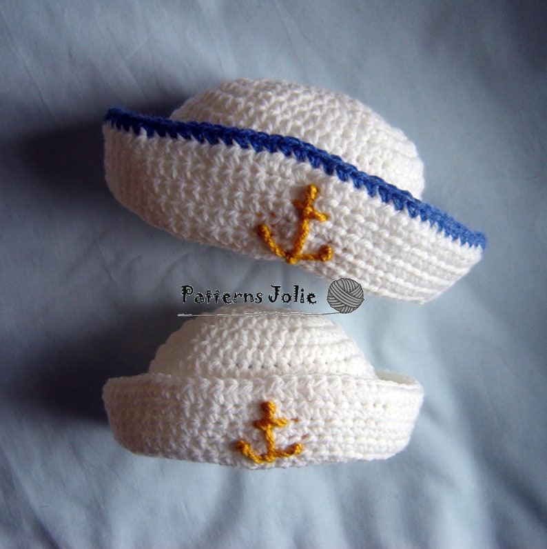 May include: Two white crocheted sailor hats with blue trim and yellow anchor embroidery. The hats are different sizes, one is larger than the other.