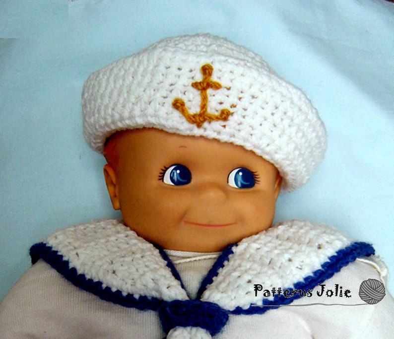 May include: A white crocheted sailor hat with a gold anchor on the front, worn by a doll with blue eyes. The doll is wearing a white crocheted sailor collar with a blue trim.