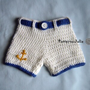 May include: White crocheted shorts with a blue crocheted belt and yellow anchor applique. The shorts have white buttons on the sides.