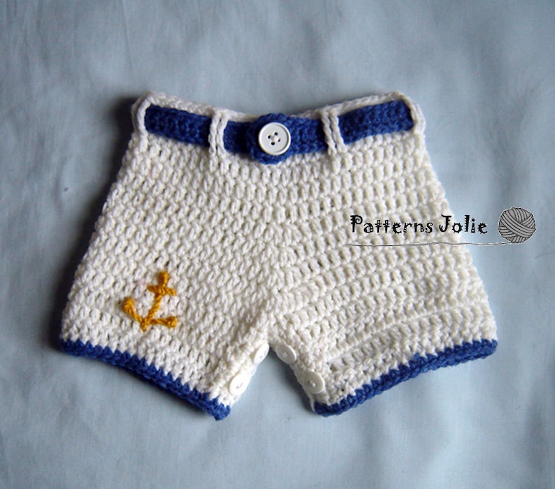May include: White crocheted shorts with a blue crocheted belt and yellow anchor applique. The shorts have white buttons on the sides.