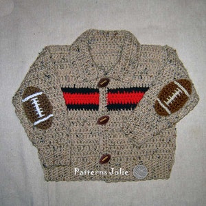 以下が含まれることがあります： 茶色、黒、赤のストライプ模様のクロシェ編みのカーディガン。カーディガンは袖にフットボールの形のアップリケと茶色のボタンが付いています。