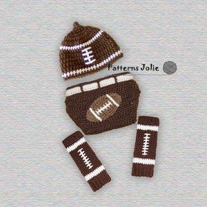 May include: A brown and white crocheted baby outfit with a football theme. The outfit includes a hat, nappy cover, and leg warmers. The hat and leg warmers have white stripes and a football design. The nappy cover has a brown football design.