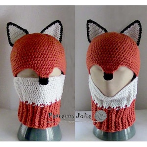 May include: A crocheted fox hat with a white face mask and orange and white stripes. The hat has black ears and a black nose.
