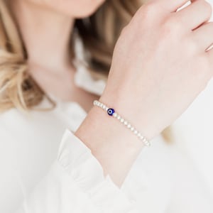 May include: A silver bracelet with a blue evil eye charm. The bracelet is made of small silver beads.