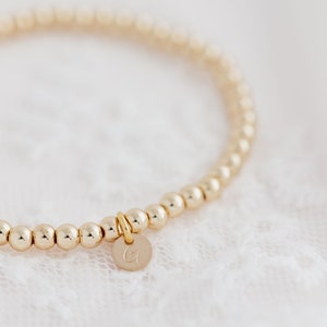 May include: A gold beaded bracelet with a small gold charm that has the letter "G" engraved on it.