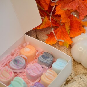 May include: A white box filled with pink tissue paper and nine small, colourful, heart-shaped wax melts. The box is open and the wax melts are visible. The box is sitting on a brown hessian surface.