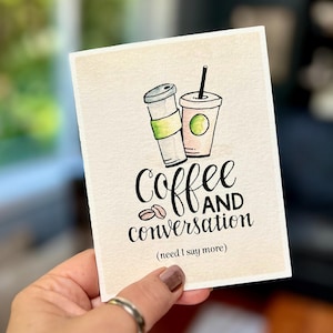 May include: A greeting card with a watercolor illustration of two coffee cups and the words "Coffee AND conversation (need I say more)" in black script. The card has a cream-colored background.