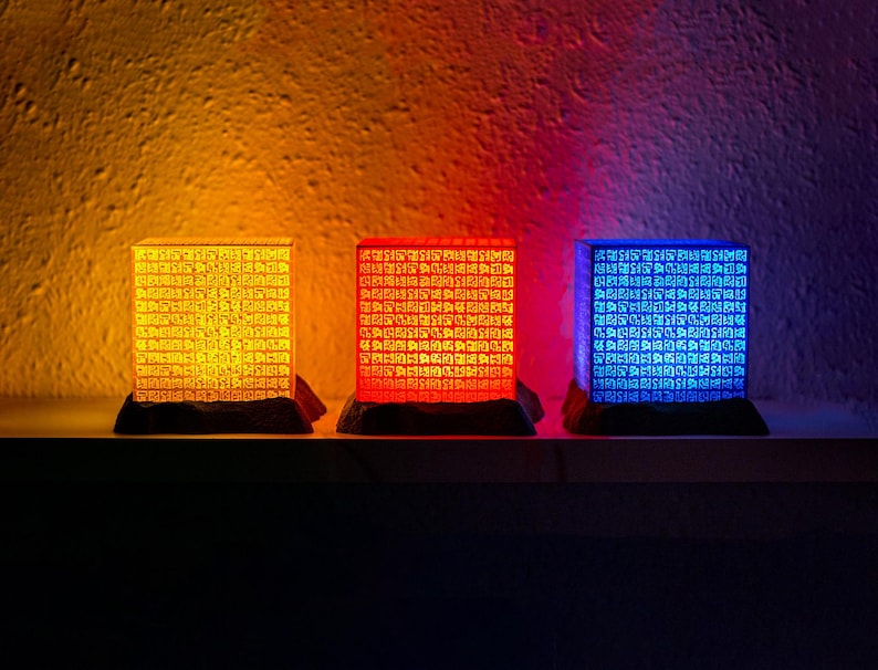 Tres poneglyphs iluminados en tonos naranja, rojo y azul descansan sobre una repisa, proyectando un aura mística y ancestral en la habitación