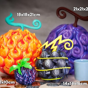 Cuatro réplicas artesanales de Frutas del Diablo de One Piece agrupadas sobre una mesa, con monedas decorativas a la base. A la derecha, la Gomu Gomu no Mi púrpura gigante de 21 × 21 × 24 cm; a la izquierda, la Mera Mera no Mi anaranjada con llamas de 18 × 18 × 21 cm. Delante, la Jiki Jiki no Mi gris-metal con relámpago amarillo y pinchos (14 × 14 × 16 cm) y la pequeña fruta Yami Yami No Mi de 8 × 8 × 10 cm. Todas pintadas a mano, ideales para cosplay y decoración.