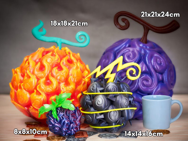 Cuatro réplicas artesanales de Frutas del Diablo de One Piece agrupadas sobre una mesa, con monedas decorativas a la base. A la derecha, la Gomu Gomu no Mi púrpura gigante de 21 × 21 × 24 cm; a la izquierda, la Mera Mera no Mi anaranjada con llamas de 18 × 18 × 21 cm. Delante, la Jiki Jiki no Mi gris-metal con relámpago amarillo y pinchos (14 × 14 × 16 cm) y la pequeña fruta Yami Yami No Mi de 8 × 8 × 10 cm. Todas pintadas a mano, ideales para cosplay y decoración.