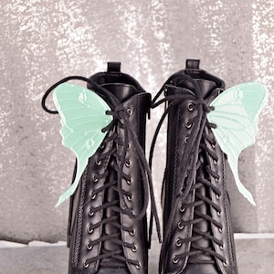 May include: A pair of black lace-up boots with green butterfly-shaped shoe charms attached to the laces.