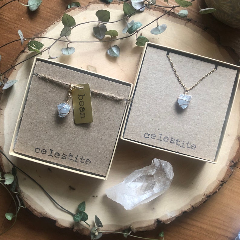 K&ouml;nnte beinhalten: Zwei Schmuckschatullen mit dem Aufdruck "Celestit". Eine Schatulle enth&auml;lt einen goldfarbenen Ohrring mit einem hellblauen Stein, die andere eine goldfarbene Halskette mit einem &auml;hnlichen Stein. Ein klarer Kristall ist ebenfalls vorhanden. Das Wort "bean" steht auf einem Anh&auml;nger.