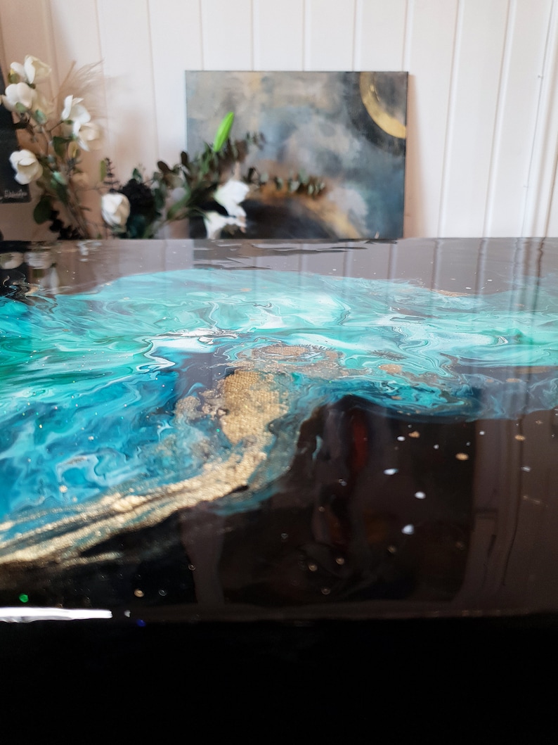 Puede incluir: Primer plano de una mesa de resina negra con un dise&ntilde;o abstracto azul, verde y dorado. El dise&ntilde;o se asemeja a un oc&eacute;ano arremolinado con acentos dorados.