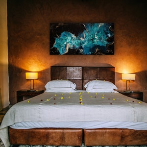 Puede incluir: Una cama blanca con una cabecera de cuero marr&oacute;n y un edred&oacute;n blanco. La cama est&aacute; decorada con p&eacute;talos de flores amarillas y rojas. Hay una gran pintura abstracta sobre la cama y dos l&aacute;mparas en mesitas de noche a ambos lados de la cama.
