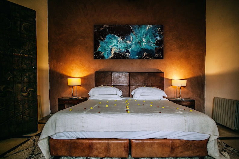 Puede incluir: Una cama blanca con una cabecera de cuero marr&oacute;n y un edred&oacute;n blanco. La cama est&aacute; decorada con p&eacute;talos de flores amarillas y rojas. Hay una gran pintura abstracta sobre la cama y dos l&aacute;mparas en mesitas de noche a ambos lados de la cama.