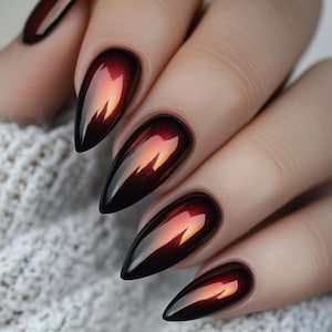May include: Close-up of a hand with long, pointed nails. The nails are painted with a gradient effect, transitioning from a deep black at the base to a fiery red and orange at the tips, creating a glossy, reflective finish.
