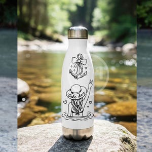 Puede incluir: Una botella de agua de acero inoxidable blanca con tapa y base de metal plateado. El frente presenta un dise&ntilde;o de l&iacute;neas negras de un ancla con un lazo sobre una persona con sombrero de sol en el agua, con el texto "lake day" y corazones.