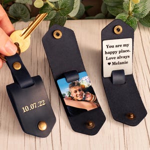 May include: Three dark navy blue leather key organizers with gold-tone metal snaps. One shows the date 10.07.22 embossed on the exterior. Another displays a color photograph of a couple. The third reveals an interior tag with the text: You are my happy place. Love always Melanie.