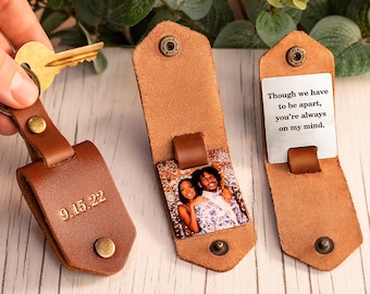 May include: Three brown leather keychains with metal snap closures. One keychain shows the date 9.15.22 embossed on the exterior. Another displays a color photograph of a couple, and the third features a metal plate with the text: Though we have to be apart, you're always on my mind.