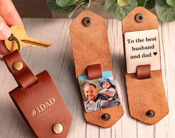 May include: Three brown leather keychains with metal snap closures. One keychain is closed and embossed with #1DAD. The second is open, revealing a square photo of a person carrying a child. The third is open, showing a metal plate with the text To the best husband and dad with a heart symbol.