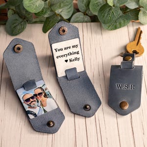 May include: Three grey leather key organizers with brass-colored snap buttons. One shows a photo of a couple, another displays the text "You are my everything Kelly" with a heart, and the third is closed and embossed with the initials "W.S.R."