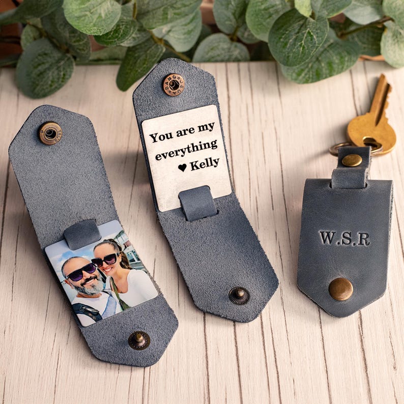 May include: Three grey leather key organizers with brass-colored snap buttons. One shows a photo of a couple, another displays the text "You are my everything Kelly" with a heart, and the third is closed and embossed with the initials "W.S.R."