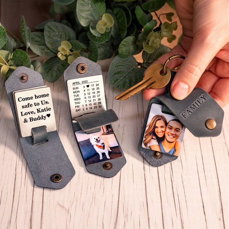 May include: Three gray leather keychains with brass snaps. One features a metal plate with the text 'Come home safe to Us. Love, Katie & Buddy'. Another shows an April 2022 calendar and a dog photo. The third displays a couple's photo and 'FAMILY'.