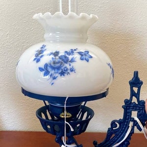 May include: A blue and white oil lamp with a floral design on the glass shade. The lamp is attached to a blue metal wall mount. The lamp has a price tag that reads "Distinctively designed for... #360".