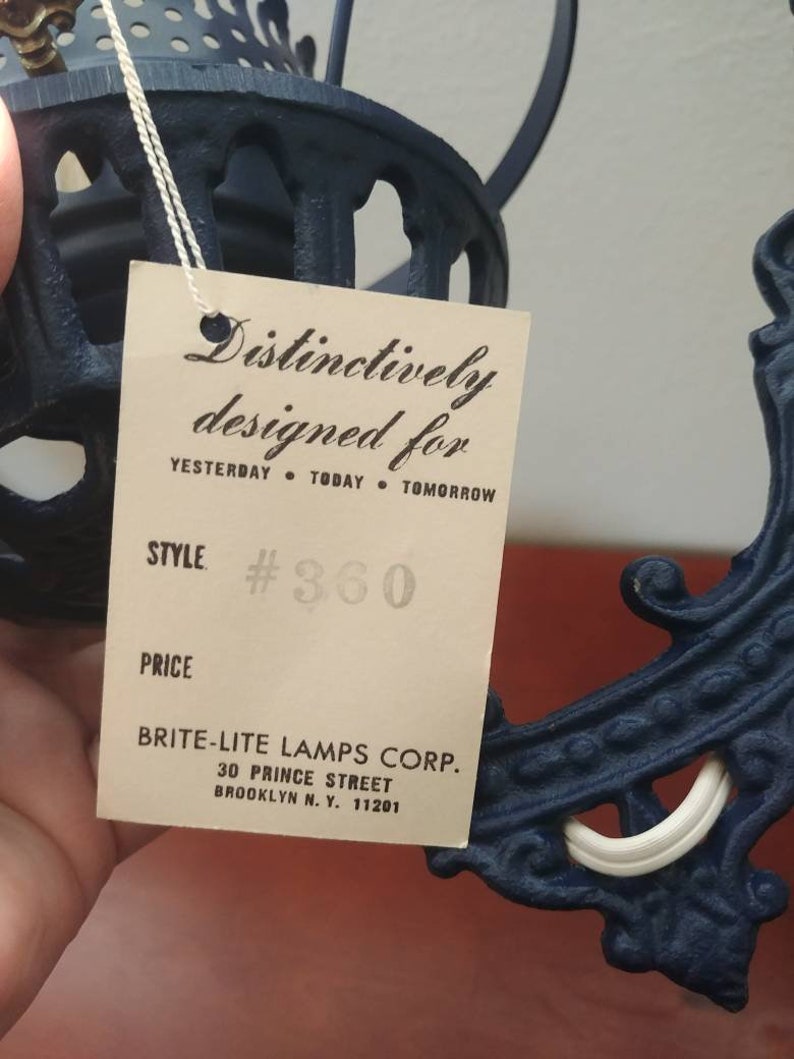 May include: A black metal lamp with a white porcelain socket and a tag that reads "Distinctively designed for Yesterday Today Tomorrow" and "Style #360". The tag also includes the company name "Brite-Lite Lamps Corp." and address "30 Prince Street Brooklyn N.Y. 11201".