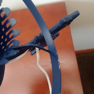May include: A blue metal lamp base with a decorative design. The base has a circular shape and a white cord.
