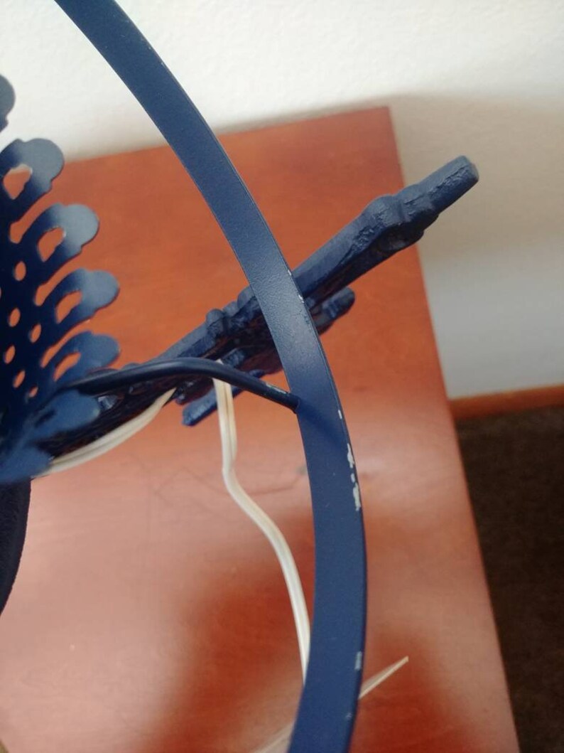 May include: A blue metal lamp base with a decorative design. The base has a circular shape and a white cord.
