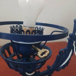 May include: A blue and white cast iron wall sconce with a keyhole and a light bulb. The sconce has a decorative design and is in good condition.
