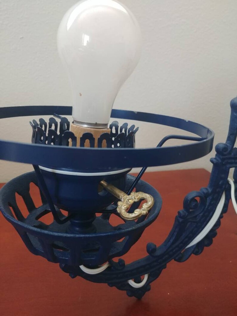 May include: A blue and white cast iron wall sconce with a keyhole and a light bulb. The sconce has a decorative design and is in good condition.