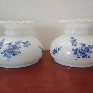 May include: Two white glass lampshades with a blue floral pattern. The lampshades have a scalloped edge.