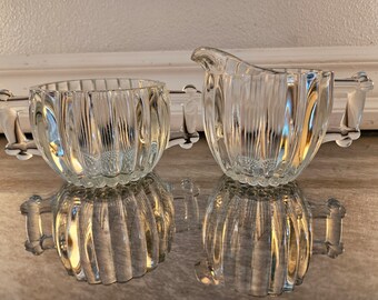 Peut inclure: Un ensemble sucrier et crémier en verre transparent avec des côtés et des poignées cannelés. L'ensemble est en verre transparent et a un aspect vintage.