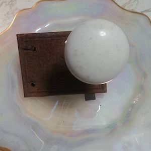 May include: White ceramic door knob with a brown metal backplate. The knob is slightly worn and has a few small scratches.