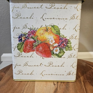 May include: A rectangular white metal container with a gold rim and lid. The container features a fruit illustration with strawberries, a peach, and blackberries. Gold script reads "Sweet Peach" and "Peach. Luscious St."