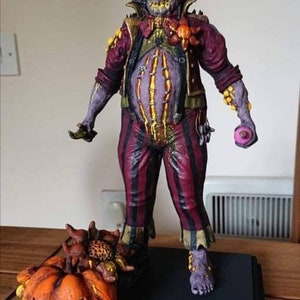 May include: A creepy clown figurine with a purple and red costume, a large belly, and a pumpkin with a scary face. The clown is holding a pink donut in one hand and a small object in the other.