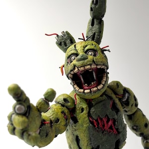 May include: A green, weathered, animatronic-style figure with a textured, decaying surface. The character features a wide-open mouth revealing inner mechanical details, one long ear, and exposed red wires throughout its damaged, segmented body.