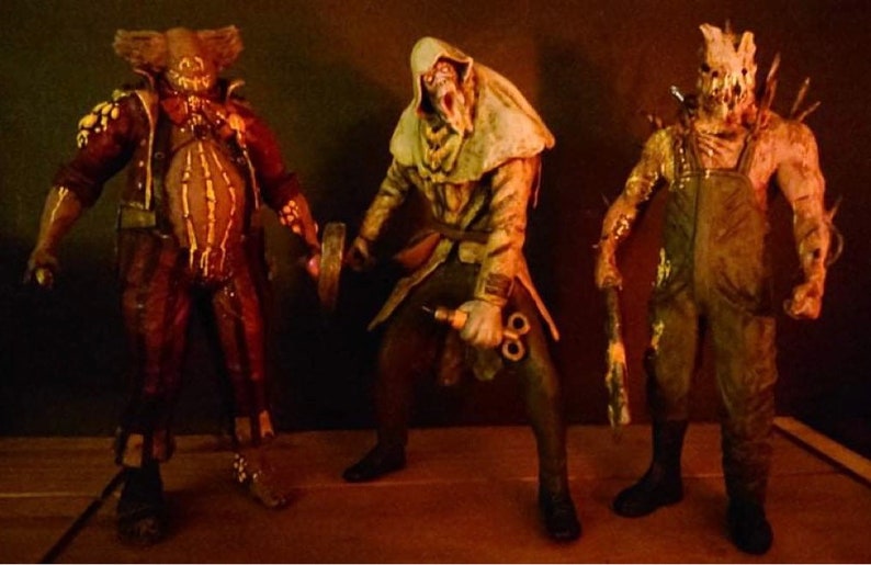 May include: Three horror movie character action figures. The figures are made of plastic and are painted in realistic detail. The figures are posed in a menacing way. The figure on the left is wearing a brown and red costume with a mask. The figure in the middle is wearing a white hooded robe and holding a syringe. The figure on the right is wearing a brown jumpsuit and a mask with a jagged mouth.
