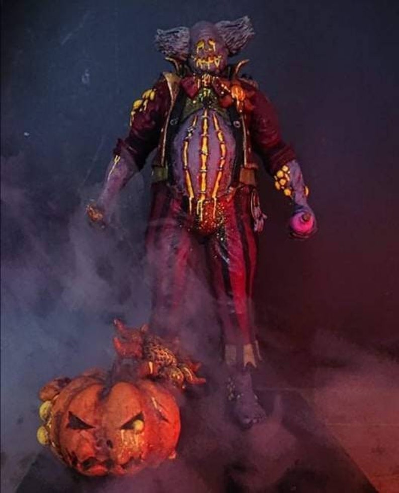 May include: A creepy clown figure with a purple and red costume, a jack-o-lantern face, and a pumpkin in front of it. The clown is holding a purple orb in its hand. The background is dark and smoky.