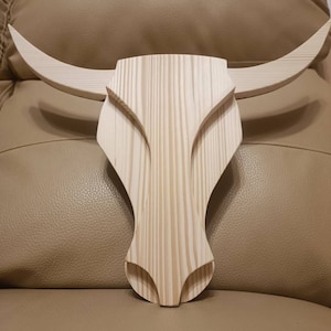 Può includere: Decorazione da parete a forma di teschio di toro in legno chiaro. Le corna curve e il design presentano un volto stilizzato e dettagliato. Il legno mostra motivi di venature visibili. Questo pezzo rustico è adatto per la decorazione della casa o dell'ufficio.
