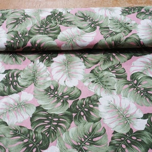 May include: Pink fabric with a green and white tropical leaf pattern. The leaves are large and have a detailed design.
