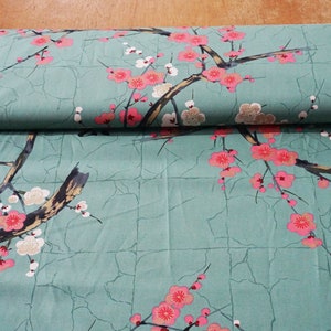 Könnte beinhalten: Ein blaugrüner Stoff mit japanisch inspiriertem Design, das rosa und weiße Blüten auf Ästen zeigt. Der Stoff hat eine subtile, rissige Textur und der Text "蓮" ist in der oberen rechten Ecke gedruckt.