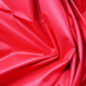 Puede incluir: Primer plano de una tela lisa de color rojo con textura sedosa. La tela está drapeada y doblada, creando líneas suaves y fluidas.
