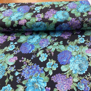 Könnte beinhalten: Eine Rolle Stoff mit floralem Muster, das große blaue und violette Blumen und grüne Blätter auf schwarzem Hintergrund zeigt. Der Stoff ist ausgerollt und zeigt das detaillierte Blumenmuster. Der Stoff ist wahrscheinlich Baumwolle oder ein ähnliches Material.