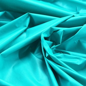 May include: Close-up of turquoise fabric with soft folds and a subtle sheen. The fabric appears smooth and lightweight, with highlights and shadows creating depth. The material is likely suitable for clothing or decorative projects.