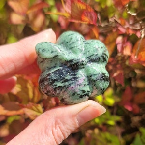May include: A green, black and pink carved gemstone with a starburst shape.