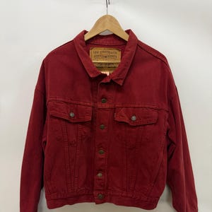 Op de afbeelding: Bordeaux spijkerjasje met een knoopsluiting, twee borstzakken en een kraag. De jas heeft een Levi Strauss & Co. label. De jas hangt aan een houten hanger tegen een witte achtergrond.