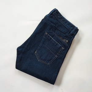 Puede incluir: Un par de pantalones vaqueros de mezclilla azul oscuro doblados sobre un fondo blanco.